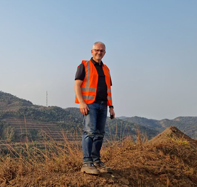 Richard wearing a bright vest standing on a hill at a reclaimed dam under development.