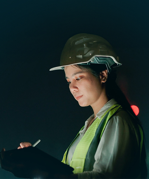 Woman wearing a hardhat writing on a tablet. 