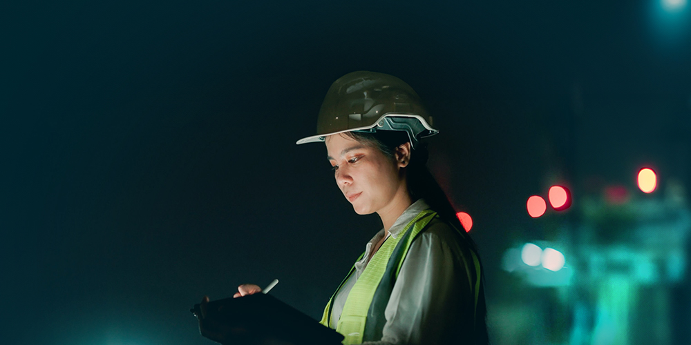 Woman wearing a hardhat writing on a tablet. 