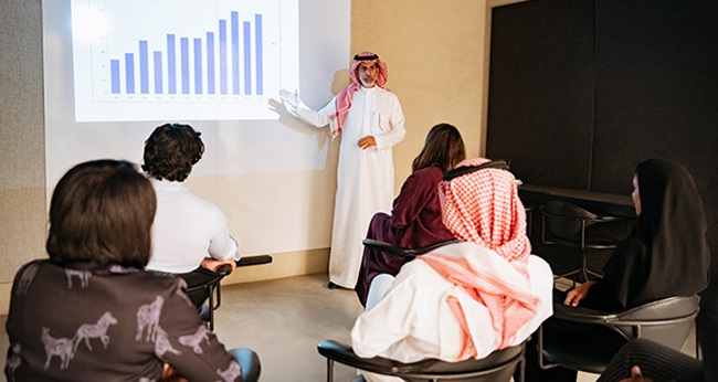 A group of Saudi nationals in a meeting room watching a presentation.