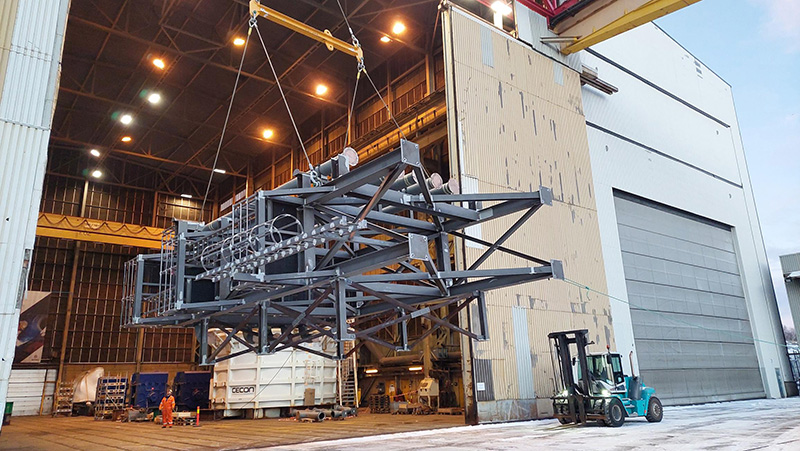 Floating Storage Regasification Unit being lifted by a crane out of a factory.