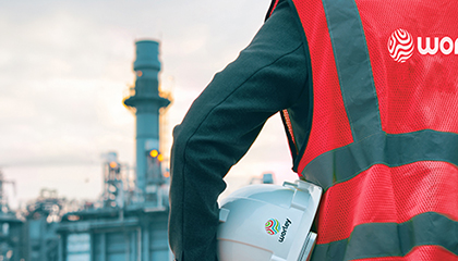 Back of a person holding a hard hat under arm, facing a refining plant.
